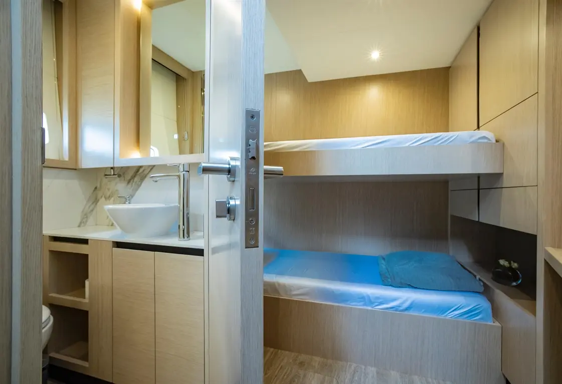 Modern cabin interior with bunk beds, a washbasin, and cabinetry, featuring wooden finishes and ample lighting.